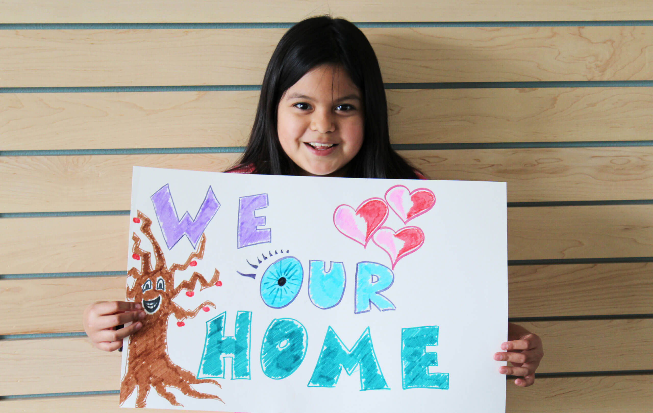 Small child holding sign that read 'We our home'