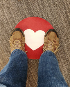 Two feet stand on a heart-shaped floor sticker for physical distancing.
