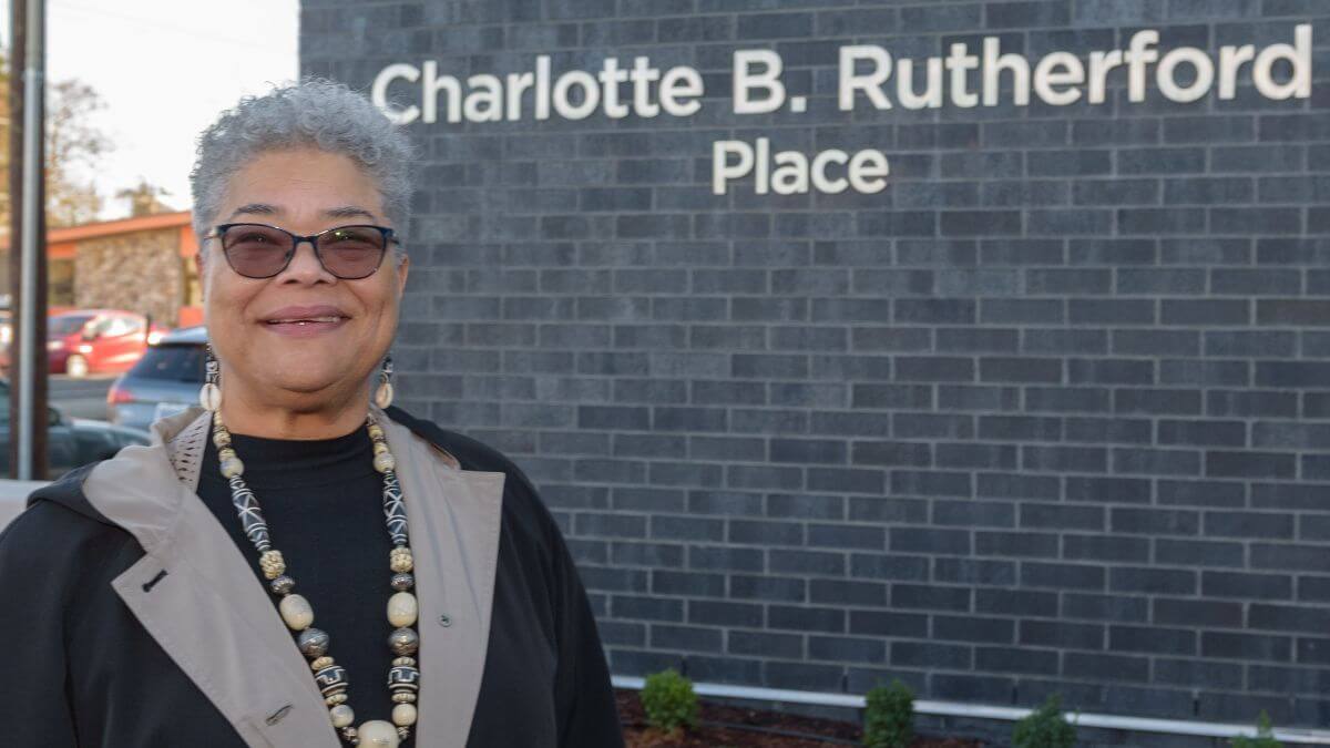 Older woman standing in front of Charlotte B. Rutherford Place sign and building