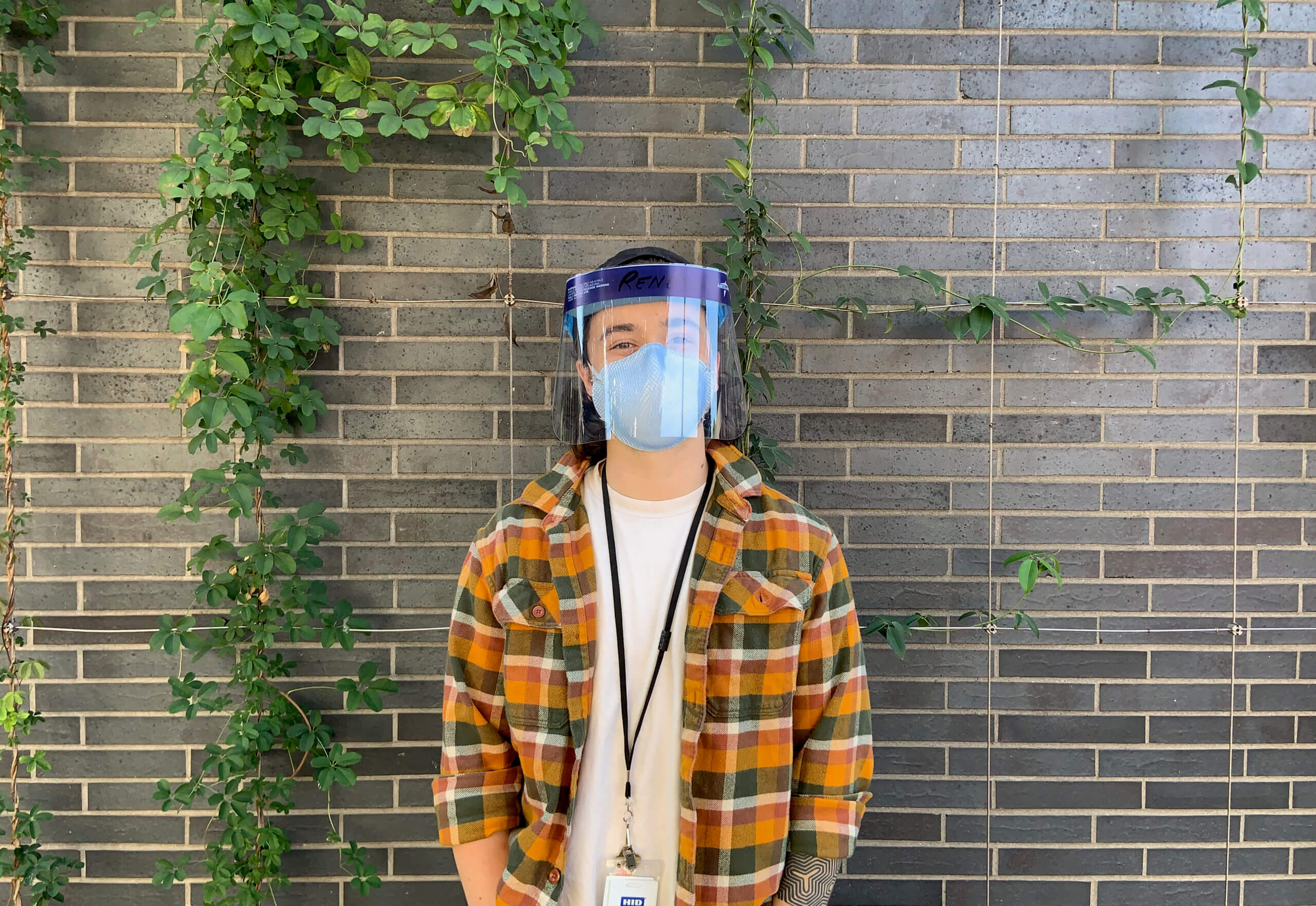 Person standing in front of brick wall wearing a face shield and mask