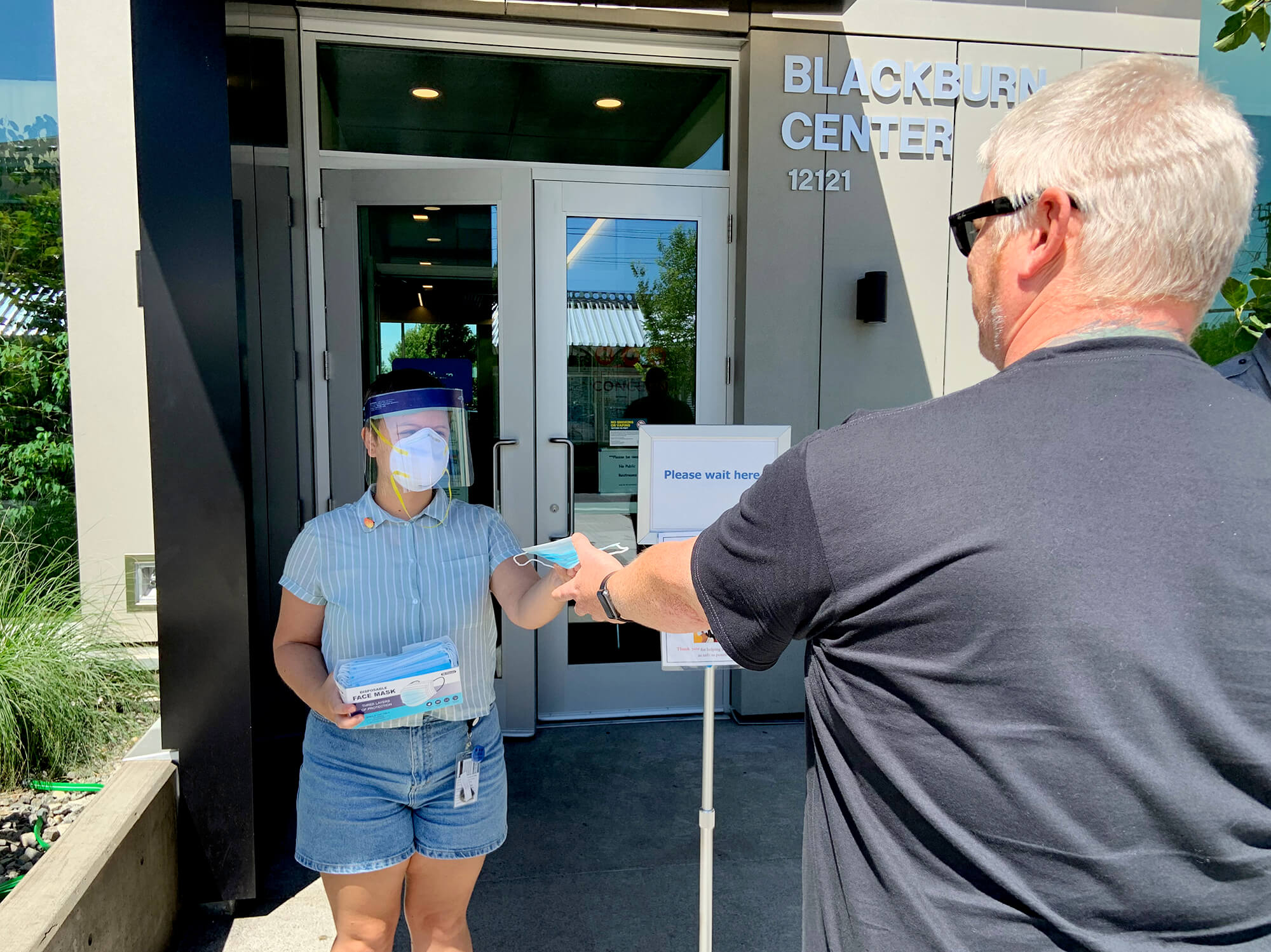 A COVID-screener greets a patient outside of Blackburn Center with a mask.