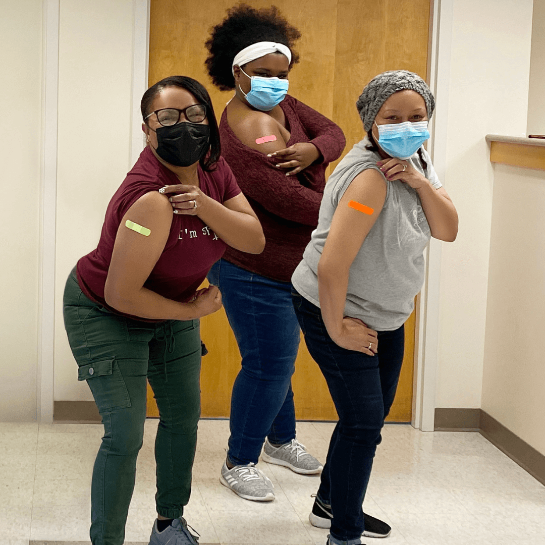 Three women show off their arms after receiving COVID-19 vaccinations.